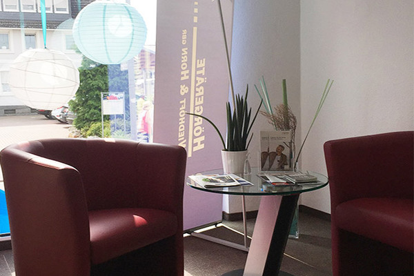 Modernes Wartezimmer mit roten Sesseln, Glastisch, Pflanzen und Informationsbroschüren.